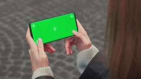 Young Woman Holding Chroma Key Green Screen with Marking Smartphone Playing Games outside city