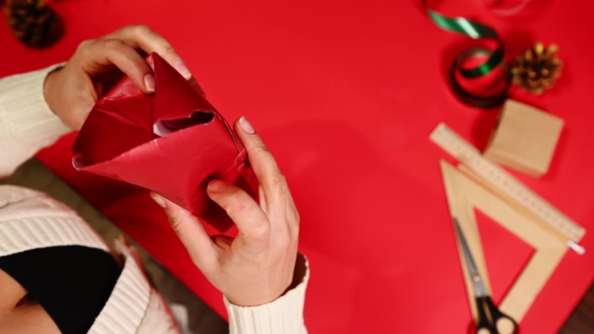 Unsuccessfully sealed the Christmas present into a red wrapping paper, that broke during packaging. Top view of a woman who damaged and torn a gift wrapping paper while packing a gift. Paper damage