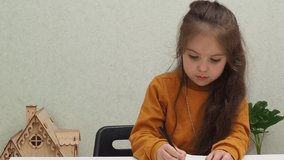Small preschooler girl sit at desk study online on phone, smart little kid wear learning using internet lessons on quarantine, homeschooling. Draws with felt-tip pens and colored pencils, imagination.