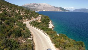 Drone following the car moving by the sea curved road near a tranquille waves on the Greek coast on Cephalonia island. Transportation, nature 4K aerial video concept.