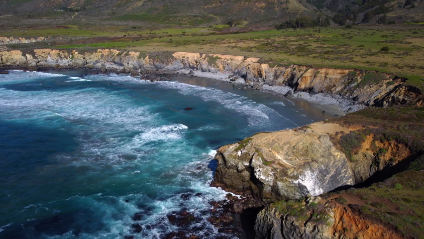 Natural Aerial drone flying over Big Sur California coast beach. The ocean clouds sky sun sunny waves crashing. Travel view scene peak weather wave. Rocky formations. High quality 4k footage.
