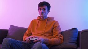 Young gamer man playing video game on TV with modern console in neon light