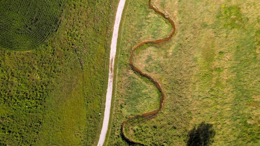 A stream spirals near a gravel path walking trail during summer in rural wisconsin - near green bay.