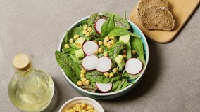 Healthy salad with a mix of lettuce leaves, radishes, avocado and chickpeas, close-up. Smooth turn
