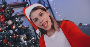 Beautiful young woman on video call invites her friends to Christmas party at her house.