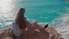 A young woman is sitting on a rock above the sea. The girl admires the seascape. Turquoise sea view from the top. The tourist destination is Turkey, Antalya.