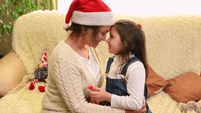 Loving mother in Santa's hat, stroking and hugging her lovely daughter, sitting together on a sofa in the living room. Happy family relationships. Carefree childhood. Christmas atmosphere at home - Powered by Shutterstock - Get 15% off with code: PIKWIZARD15