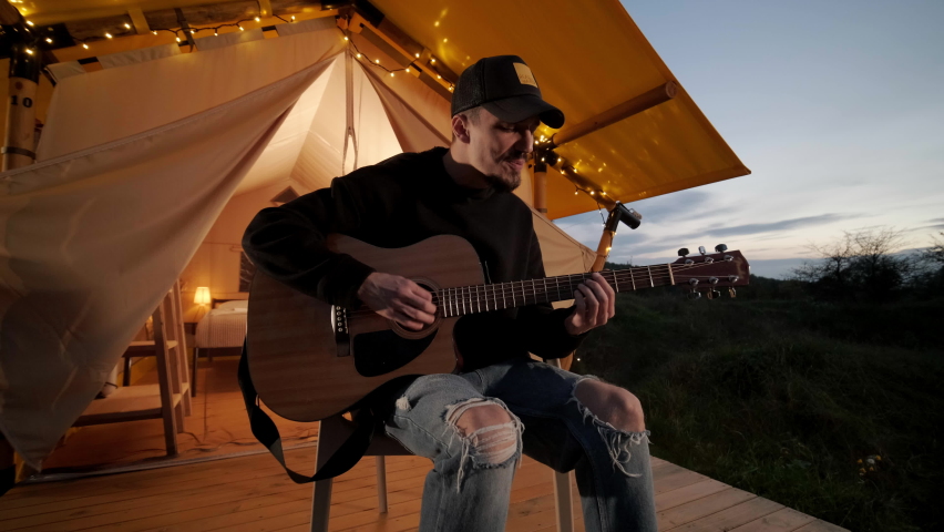Man plays the guitar and sings songs in a tent with light bulbs
