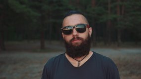 Portrait of a young hipster man with a beard and in stylish glasses on the background of the forest on a summer day