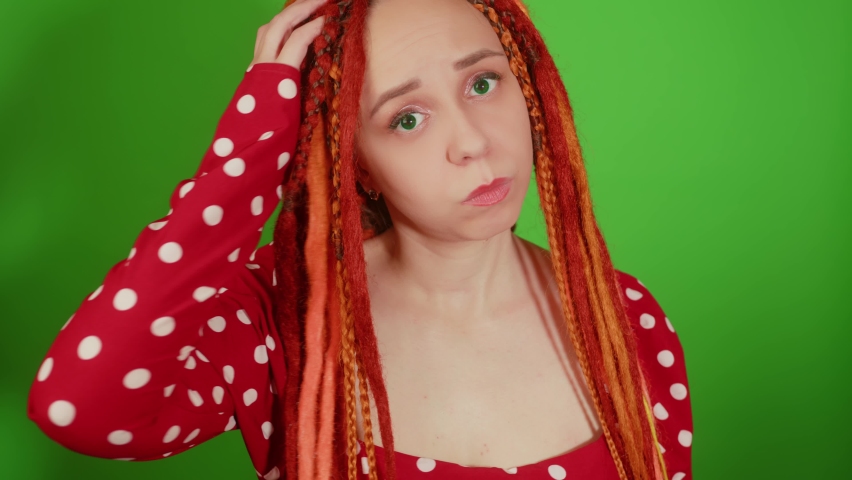 Thoughtful young woman with dreadlocks scratching head on green background. Portrait of pensive female with doubt glance looking at camera. Royalty-Free Stock Footage #1096768747