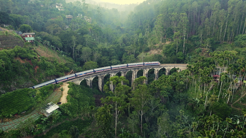 Aerial view of a train riding at dawn over the Nine Arches Bridge in Sri Lanka, surrounded by lush green scenery, tea plantations and hills Royalty-Free Stock Footage #1096775537