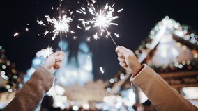Celebrating New Year Christmas holidays vacation. Friends hands closeup with sparklers in air at decorated town square. Xmas Christmas Eve winter atmosphere. Unrecognisable people holding lights wave. - Powered by Shutterstock - Get 15% off with code: PIKWIZARD15