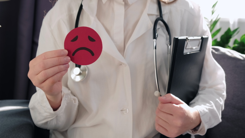 Close-up of woman doctor with stethoscope hold little red angry emoticon and clipboard sit on sofa. Emotional intelligence, balance emotion control, mental health assessment, bipolar disorder concept | Shutterstock HD Video #1096796227