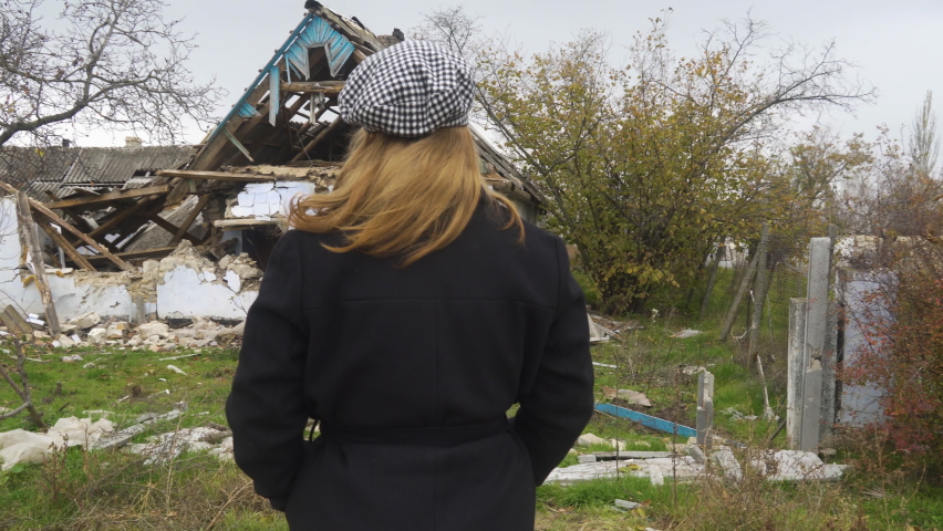 War in Ukraine. Russian invasion of Ukraine. Countryside. The girl looks at the house destroyed by shelling (panorama, the camera moves from right to left). Terror of the civilian population