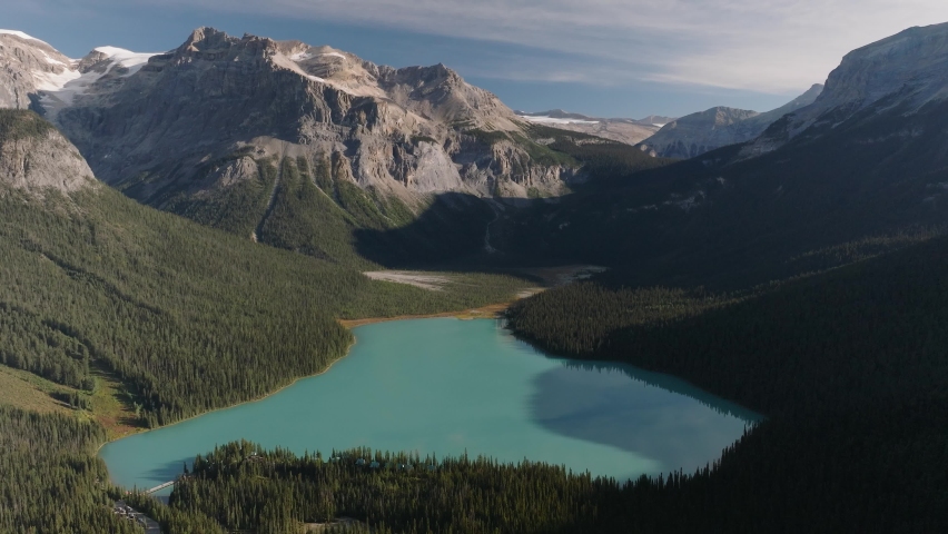 Aerial dolly out of emerald Lake Louise surrounded by dense pine tree forest and mountains at Banff National Park, Alberta, Canada Royalty-Free Stock Footage #1096800619