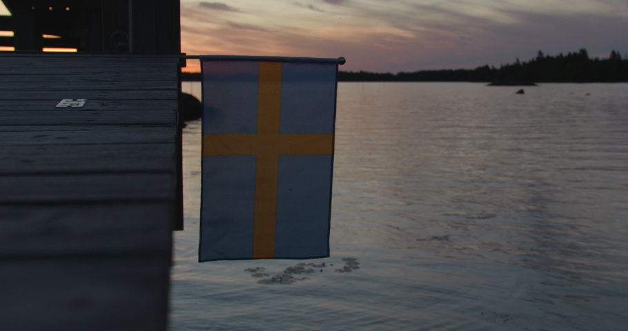 The national flag of Sweden on the wooden pier at the shore at soft sunset