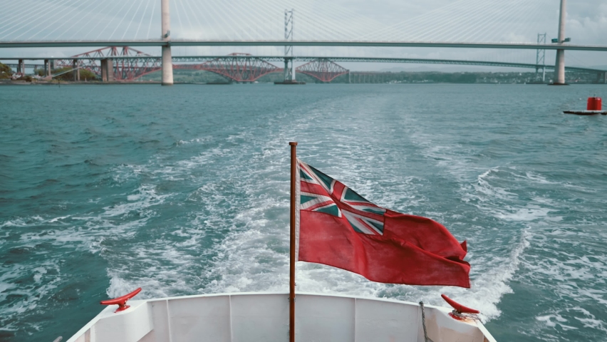 The boat moves through the river with the Red Ensign flag waving