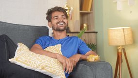 Relaxed happy young man watching tv or television by eating snacks at home - concept of leisure activity, weekend lifestyle and entertainment