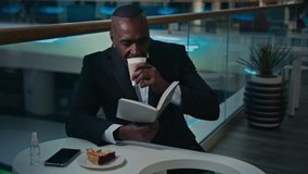 African man worker businessman employer entrepreneur sitting at table in cafe cafeteria restaurant drink aromatic coffee drinking tea latte cappuccino reading book read notebook information text study - Powered by Shutterstock - Get 15% off with code: PIKWIZARD15