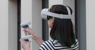 Experience VR. Young woman with virtual reality headset and motion controllers near building