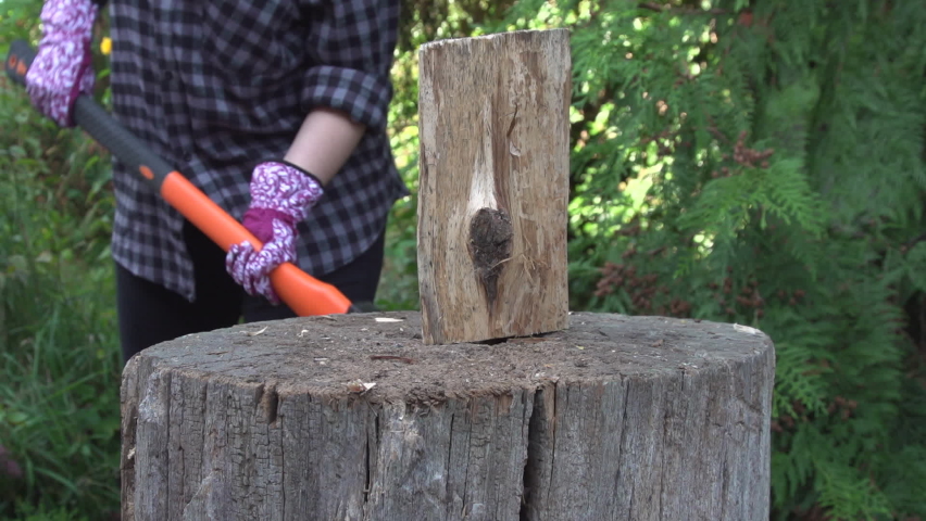 woman chopping a log wood with an ax in the garden. chop wood with a flared splitting ax. Close up slow motion