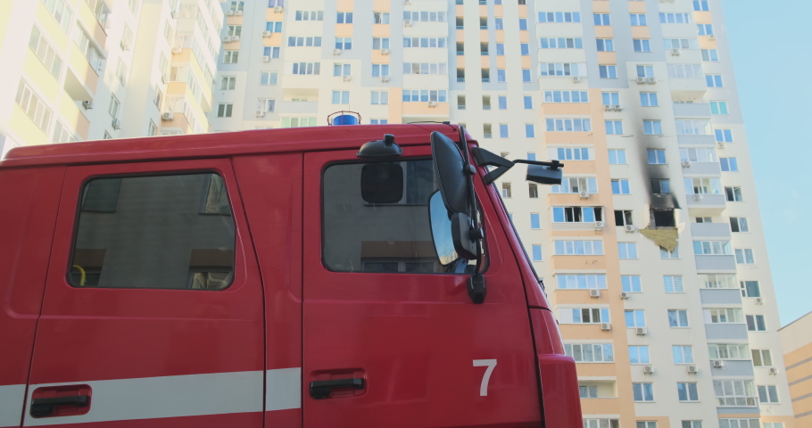 Red fire truck stands against the background of a burned-out apartment in a multi-storey residential building in
