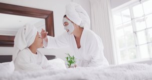 Video of happy asian mother and daughter in robes moisturizing faces and having fun. Family, motherhood, relations and spending quality time together concept digitally generated video.
