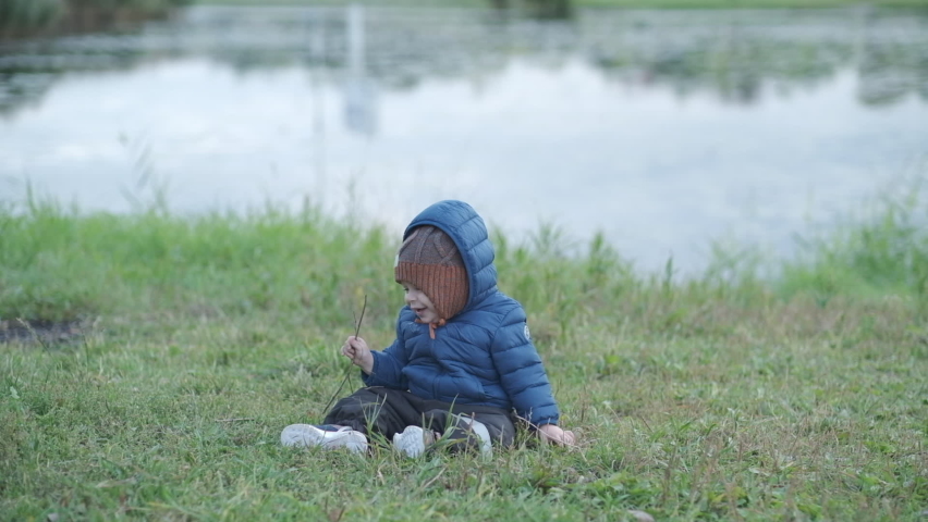 A cute toddler baby boy is playing on the ground wearing a blue jacket 