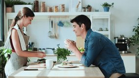 Video of happy young couple enjoying breakfast while talking in the kitchen at home.