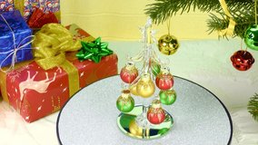 A small Christmas tree on a colored background rotates between two large Christmas trees