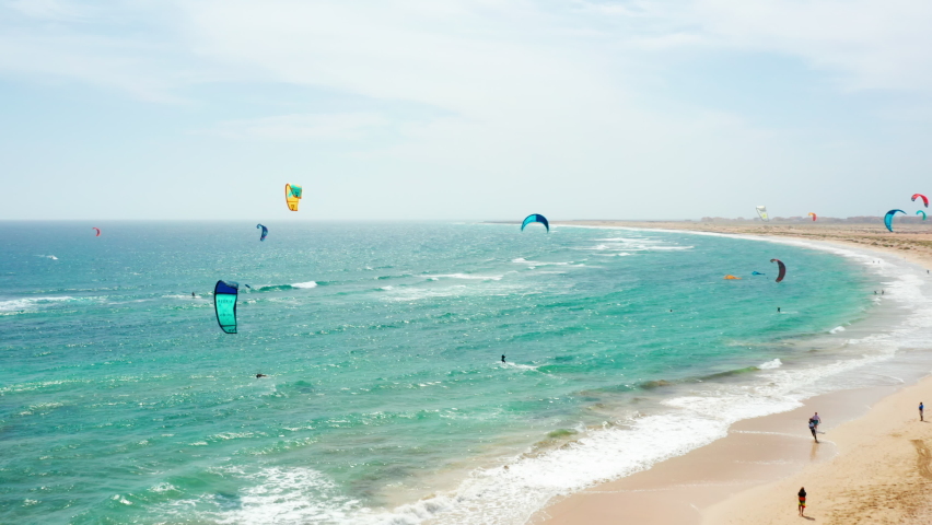 Flying over kiters in Sal, Cape Verde. Drone bird eye view over professional Kite surfers training in Cape Verde. Turquoise wavy ocean. Bright Blue Sky.