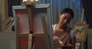 Happy youth Asia Female wear apron holding palette use brush painting on canvas create artwork cozy workshop in home at night. Contemporary Painter Abstract Modern Art, Creativity and people concept. - Powered by Shutterstock - Get 15% off with code: PIKWIZARD15