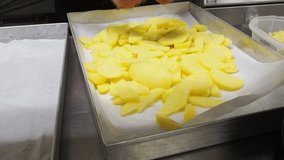 female worker in industrial kitchen slicing potatoes in oven tray to bake