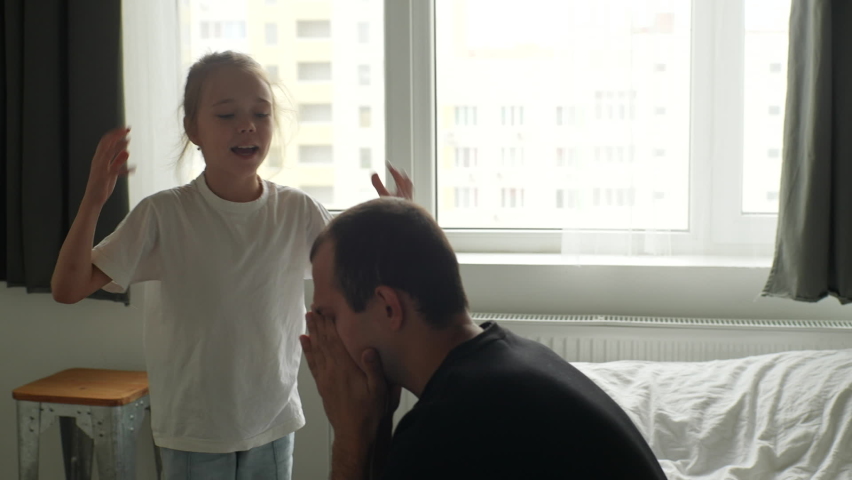 Aggressive cute preteen child daughter scolding, raising voice, screaming and gesturing with arms to sad young father sitting on sofa in dark room on background of window. Shooting in slow motion. Royalty-Free Stock Footage #1096832121