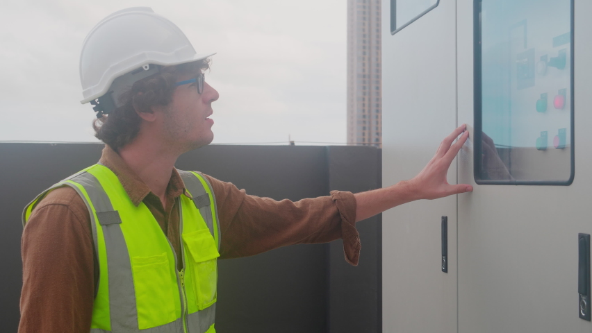 Electrical young man engineer examining maintenance cabinet system electric on rooftop and using radio for communication, one person, electrician inspection and panel control power distribution.
