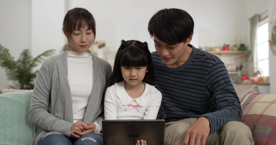 Asian daughter using tablet computer playing games with her mom and dad on living room couch at home. the smiling parents pointing at screen and sharing ideas Royalty-Free Stock Footage #1096833511