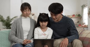Asian daughter using tablet computer playing games with her mom and dad on living room couch at home. the smiling parents pointing at screen and sharing ideas