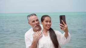 Happy adult couple walking at the beach and using a smartphone to taking a self photograph or selfie together. Happy Couple using smartphone for video call to their friends at the beach.