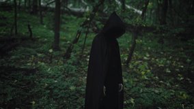 A mysterious black figure in a tunic and hood stands in the middle of a dark forest. Witch and evil in the forest. - Powered by Shutterstock - Get 15% off with code: PIKWIZARD15