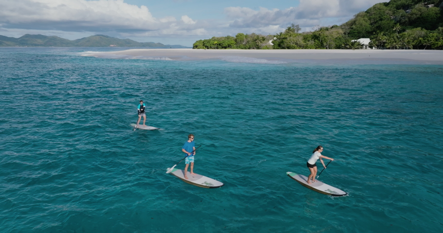 Aerial view of three people having fun on a stand up paddle board paddling around Cousine Island, Seychelles Royalty-Free Stock Footage #1096849585