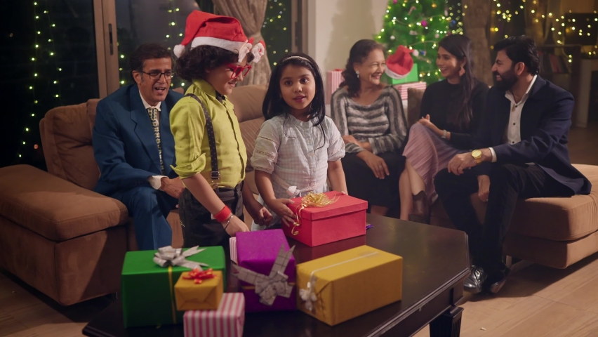 A young cute happy smiling girl and a boy surrounded by elderly family members opening gifts or goodies and having fun or enjoying together during the Christmas festival or holidays celebration Royalty-Free Stock Footage #1096853913