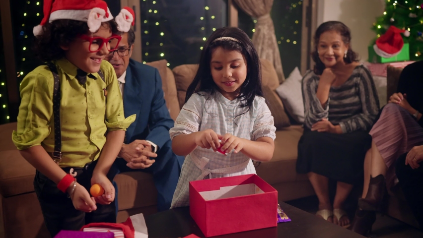 A young cute happy smiling girl and a boy surrounded by elderly family members opening gifts or goodies and having fun or enjoying together during the Christmas festival or holidays celebration Royalty-Free Stock Footage #1096853917