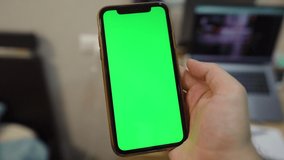 Use green screen for copy space closeup. Chroma key mock-up on smartphone in hand.  young man holds mobile phone and swipes photos or pictures left indoors of cozy home