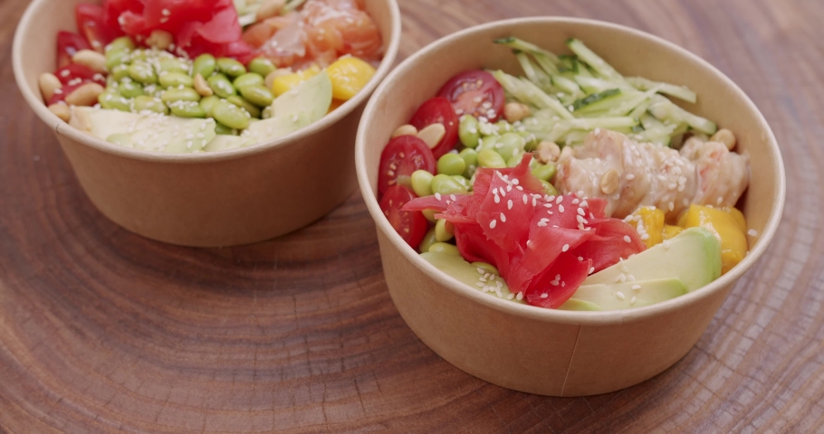 Poke bowl with salmon, shrimp, rice, avocado, edamame beans, cucumber on a wooden background. Healthy food, Asian raw meal. traditional Hawaiian raw fish salad. Poke bowl, Japanese food. Royalty-Free Stock Footage #1096862469