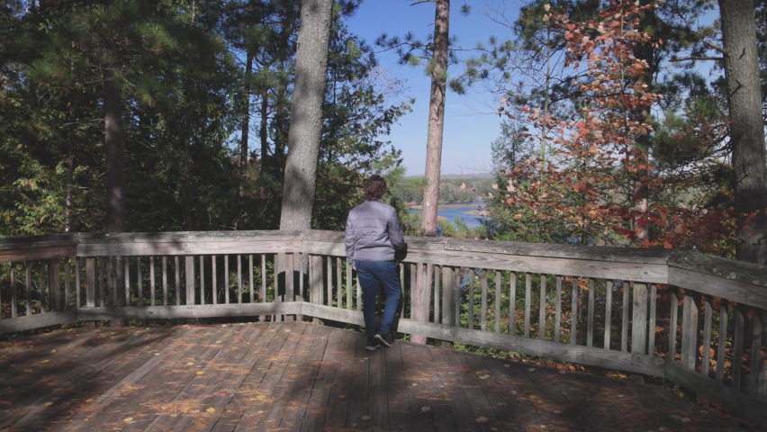 Woman looking at Au Sable River in Michigan on overlook during fall colors with gimbal video moving forward.