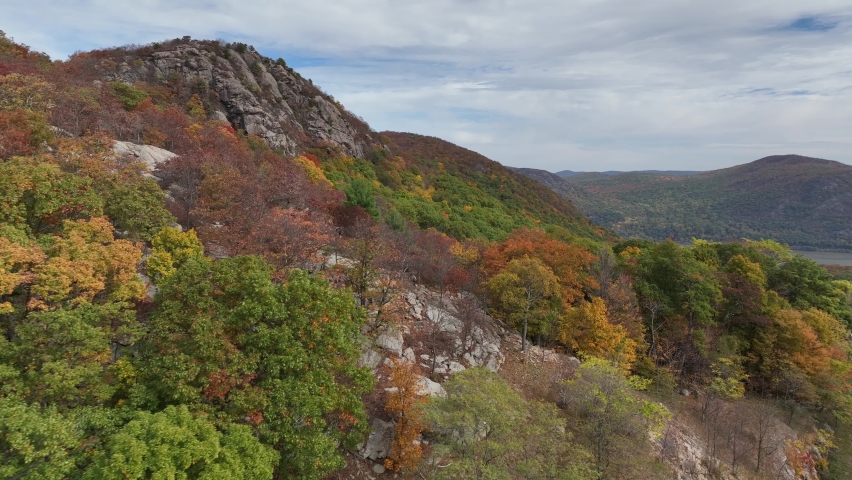 An aerial view over the mountains in upstate NY during the fall foliage change, on a beautiful day with white clouds. The camera dolly in and pan right just above the spectacular landscape.
