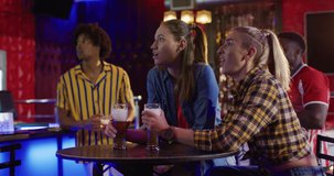 Video of diverse group of happy friends drinking and watching sports game at a bar, celebrating. Friendship, inclusivity, going out and socialising concept.