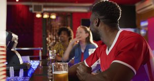 Video of diverse group of happy friends drinking and watching sports game at a bar. Friendship, inclusivity, going out and socialising concept.