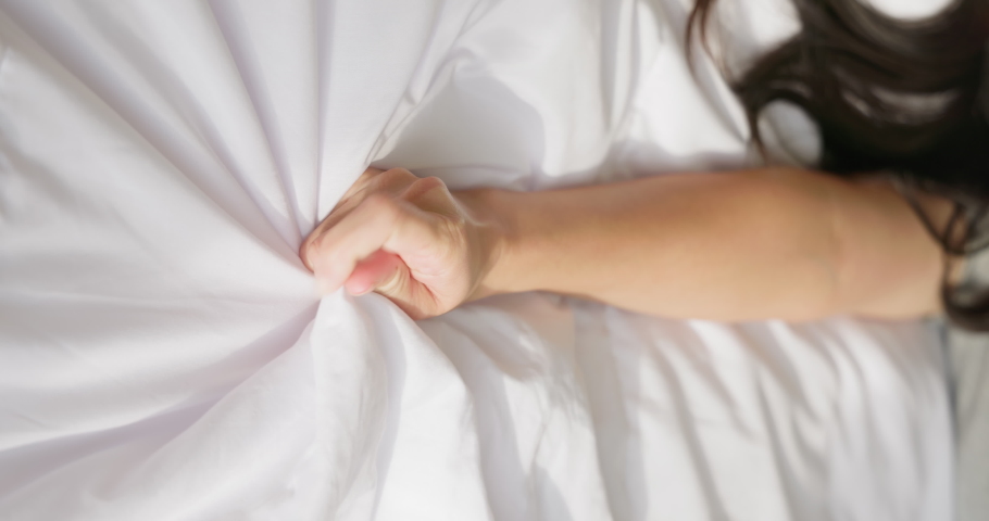 vertical close up of woman hand pulling or grasping white sheets - orgasm concept
