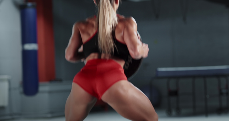 Strong muscular woman practicing sports in gym. Healthy middle-aged adult woman in black sportswear doing exercises alone. Fit girl squatting intensively indoors, training hard
